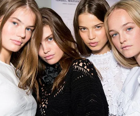 Four models with different hairstyles and colors, posing together at a fashion show, wearing various white and black outfits.