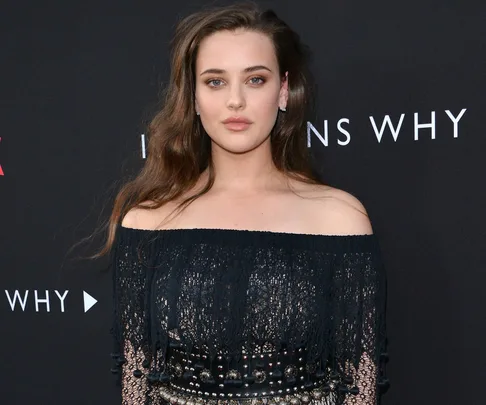 Actress in a black off-shoulder top at the premiere of "13 Reasons Why" against a black backdrop with the show's title.