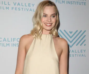 Margot Robbie in a beige halter dress at the Mill Valley Film Festival, smiling in front of a festival background.