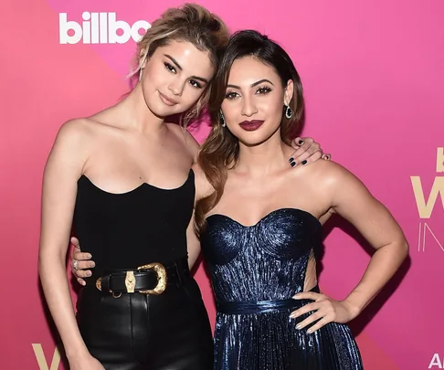 "Selena Gomez and another woman at Billboard's Woman of the Year event, posing against a pink background."