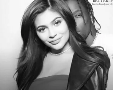 Black and white photo of a smiling woman with long hair standing in front of a man with braided hair.