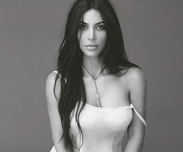 Black-and-white portrait of Kim Kardashian in a strapless white dress with long, dark hair down, looking directly at the camera.