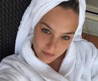 Woman wrapped in a white towel and robe, looking at the camera with a relaxed, fresh-faced appearance.