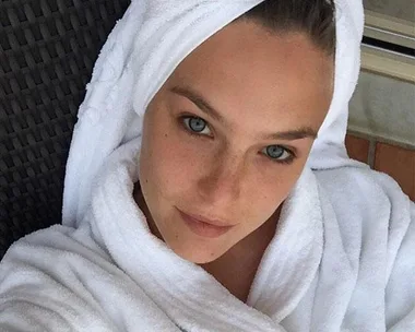 Woman wrapped in a white towel and robe, looking at the camera with a relaxed, fresh-faced appearance.