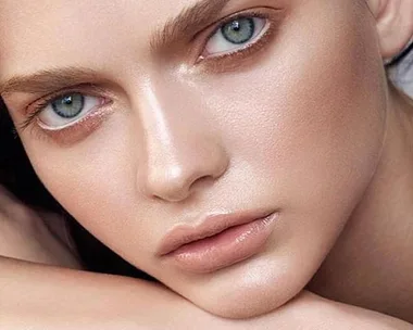 Close-up of a person's face with flawless, glowing skin, defined eyebrows, and light-colored eyes.