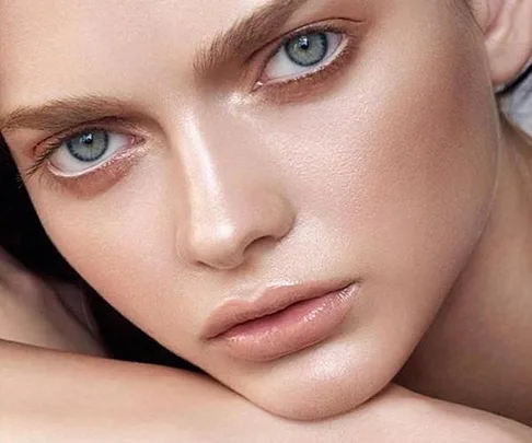 Close-up of a person's face with flawless, glowing skin, defined eyebrows, and light-colored eyes.