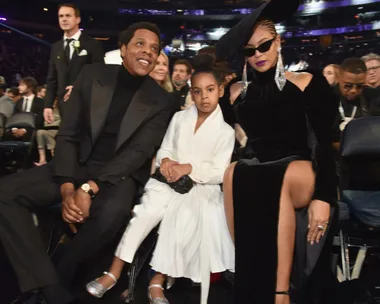 A family dressed elegantly sitting at an event, with the woman in a black outfit and hat, the man in a black suit, and the child in white.