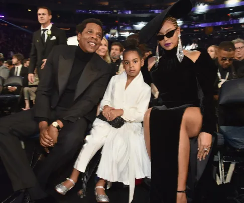 A family dressed elegantly sitting at an event, with the woman in a black outfit and hat, the man in a black suit, and the child in white.