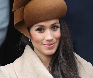 Woman with long dark hair and brown hat smiling at an outdoor event.