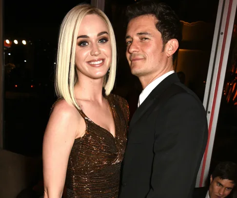 A blonde woman in a brown dress stands next to a man in a suit at a formal event.