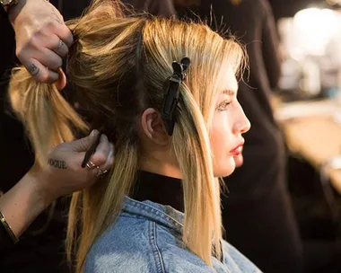 A hairdresser works on a woman's hair, styling it with clips for a reverse balayage effect.