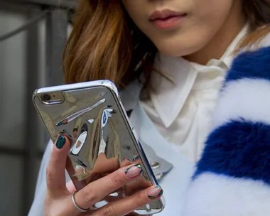 A person with metallic phone case looks at their smartphone while wearing a striped fur scarf and a white blouse.