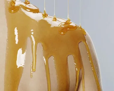 Honey being drizzled on a bare shoulder, indicating skincare treatment.