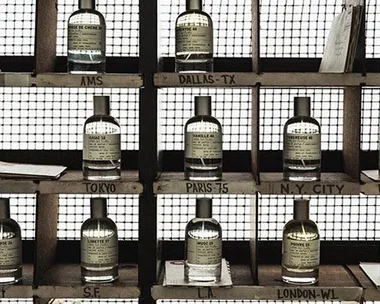 A shelf displaying various bottles of Le Labo fragrances in a grid, each labeled with different city names, like Dallas-TX and Paris-75.