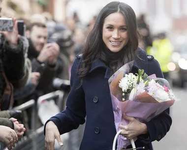 "Meghan Markle smiling, holding a bouquet of flowers while greeting a crowd."