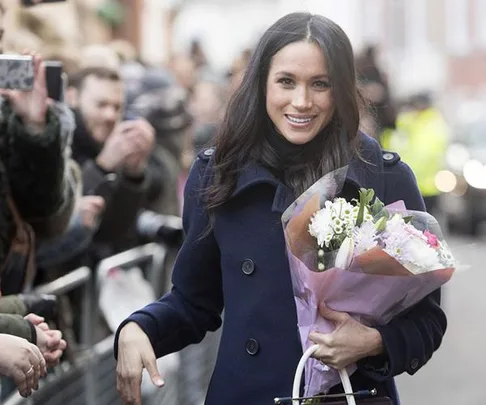 "Meghan Markle smiling, holding a bouquet of flowers while greeting a crowd."