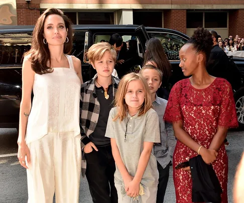 Angelina Jolie in a white outfit with four children arriving at an event, a black car in the background.