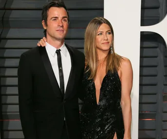 A couple dressed formally, attending a red carpet event; the woman is in a black dress and the man is in a black suit.