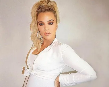 Woman in a white outfit posing with her hand on her hip, with hoop earrings and blonde hair in a ponytail.