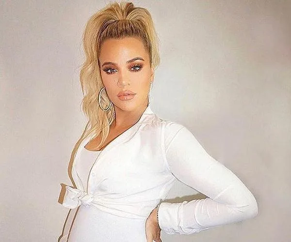 Woman in a white outfit posing with her hand on her hip, with hoop earrings and blonde hair in a ponytail.