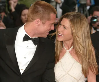 A man in a black tuxedo and a woman in a white dress are smiling at each other at a formal event.