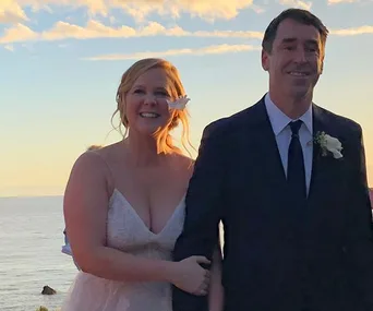 Bride and groom smiling at outdoor wedding with ocean backdrop.