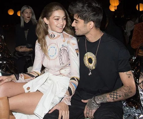 Gigi Hadid and Zayn Malik sitting close together, smiling and looking into each other's eyes at a nighttime event.