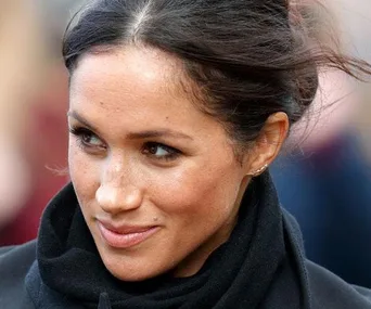 Meghan Markle smiling, wearing a black scarf, with her hair tied back.