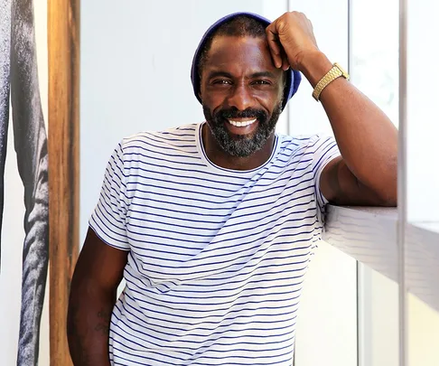 A man in a striped shirt and a beanie, leaning on a railing, smiling at the camera.