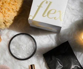 Top-down view of Flex menstrual disc packaging, a disc, a black pouch, a sponge, and beauty products on a fluffy surface.