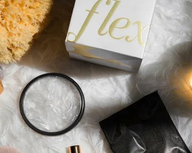 Top-down view of Flex menstrual disc packaging, a disc, a black pouch, a sponge, and beauty products on a fluffy surface.