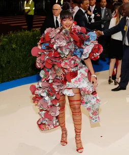 A woman in a flamboyant, floral dress with multiple layers and red strappy high heels at a formal event.