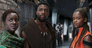 Characters Nakia, T'Challa, and Shuri from "Black Panther" are standing side by side in a tech-filled hallway.