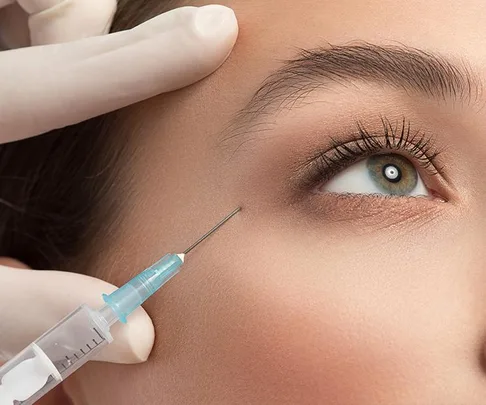 A close-up of a woman receiving an anti-aging injection near her eye, with gloved hands holding the syringe.