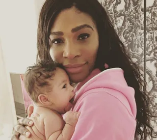 A woman in a pink hoodie holds a newborn baby. Both are looking at the camera.