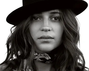 Black and white photo of a person wearing a black hat and a bandana around their neck, looking directly into the camera.