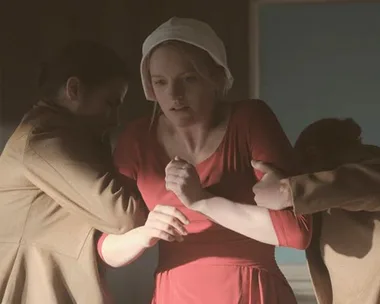 June Osborne, played by Elisabeth Moss, in The Handmaid's Tale, being forcibly held by two individuals.