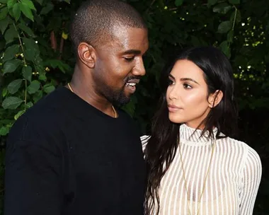 Kanye West and Kim Kardashian standing close to each other outdoors, surrounded by greenery.