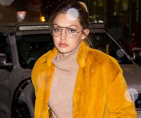 Woman in a yellow fur coat and glasses walking on a rainy night.