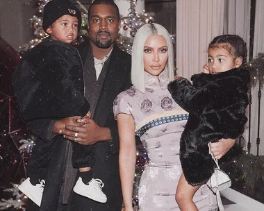 A family posing in formal attire with two children, standing in front of a decorated Christmas tree.