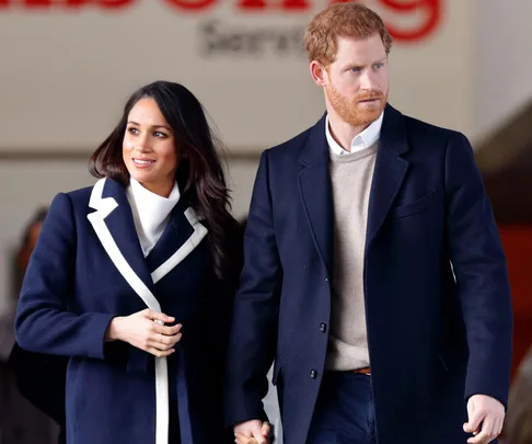 A couple holding hands, dressed in formal navy and white coats, standing together with a neutral background.