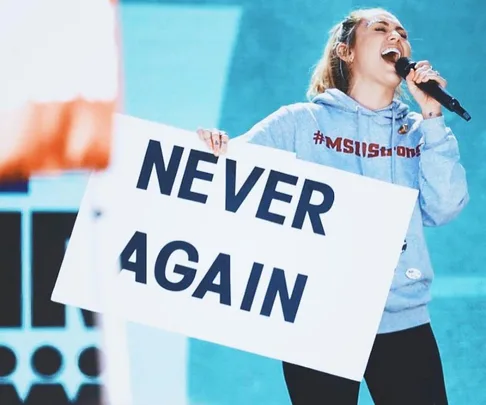 Miley Cyrus holds a "NEVER AGAIN" sign while singing at the March for Our Lives event.