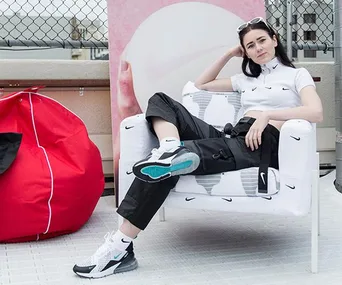 Woman in Nike outfit poses on chair with Nike logos, next to a red bean bag and a chain-link fence on a rooftop.