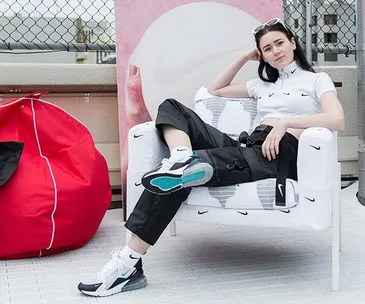 Woman in Nike outfit poses on chair with Nike logos, next to a red bean bag and a chain-link fence on a rooftop.