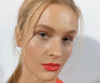 Model backstage at VAMFF 2018, with natural makeup, glossy red lips, and blonde hair tied back.