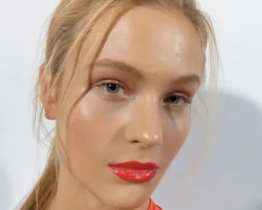 Model backstage at VAMFF 2018, with natural makeup, glossy red lips, and blonde hair tied back.