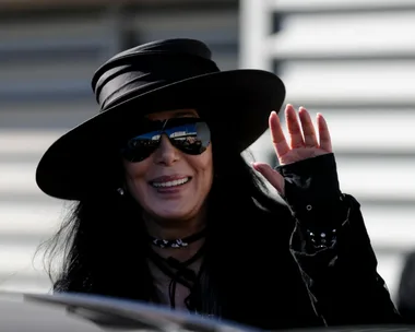 Cher wearing sunglasses and a wide-brimmed hat, waves while attending Sydney Mardi Gras 2018.