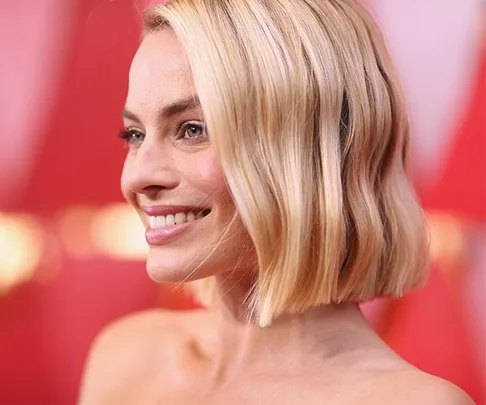 Smiling woman with short, blonde hair on the Oscars 2018 red carpet, wearing a strapless outfit.