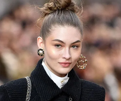 A model on the runway with hair in a high bun wearing bold statement earrings and a black coat.