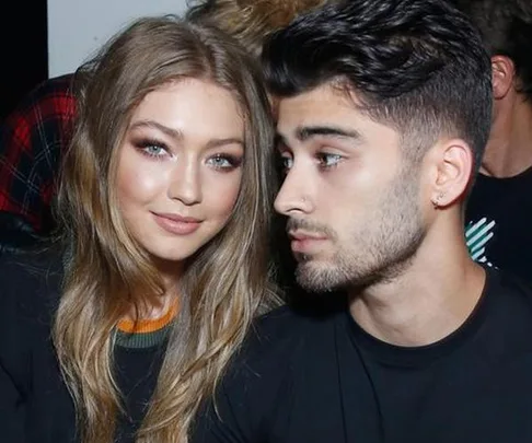 Gigi Hadid and Zayn Malik sitting together, looking at the camera, during an event.